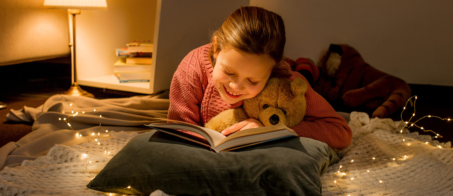 Ein kleines Mädchen liest in ihrem Bett ein Buch aus dem Verlag Egmont Publishing